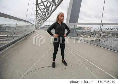 Woman in athletic wear standing confidently on a city pedestrian bridge Woman in athletic wear standing confidently on a city pedestrian bridge 130296939