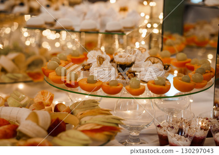 Elegant Wedding Dessert Table with Oranges, Cream Pastries, and Fruits, Warm Lighting, Celebration Feast, Luxury Event Styling, Golden Tones 130297043