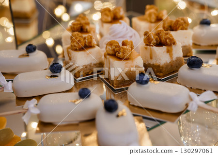 Exquisite Miniature Cheesecakes and White Chocolate Desserts Displayed on a Mirrored Tray with Decorative Blueberries 130297061