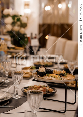 Elegant Wedding Table Setting with Appetizers and Crystal Glassware. Luxurious Reception Dinner with White Flowers, Marble Table, and Warm Lighting Elegant Wedding Table Setting with Appetizers and Crystal Glassware. Luxurious Reception Dinner with White Flowers, Marble Table, and Warm Lighting 130297099