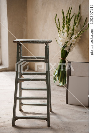Rustic Green Ladder with White Gladiolus Flowers in Glass Vase Against Textured Beige Wall, Minimalist Still Life Composition Rustic Green Ladder with White Gladiolus Flowers in Glass Vase Against Textured Beige Wall, Minimalist Still Life Composition 130297112