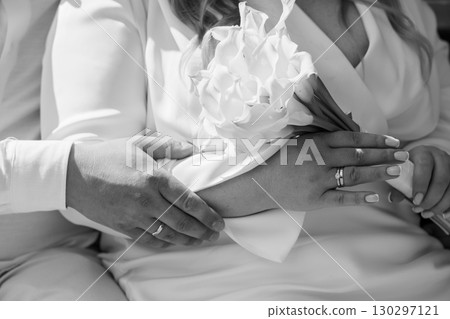 Intimate Wedding Moment: Hands Holding Flowers, Silver Wedding Bands, Romantic Couple, Black and White Photography, Soft Focus, Celebration. 130297121