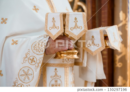 Eastern Orthodox Priest Holding Golden Chalice During Religious Ceremony in Church with Intricate Vestments. Eastern Orthodox Priest Holding Golden Chalice During Religious Ceremony in Church with Intricate Vestments. 130297196
