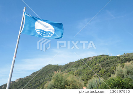 Blue flag on beach by sea. Nature and ecology, sky. Mountains and landscape of Liguria, Italy. 130297950