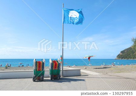 Blue flag on beach by sea. Nature and ecology, sky. Mountains and landscape of Liguria, Italy. 130297955