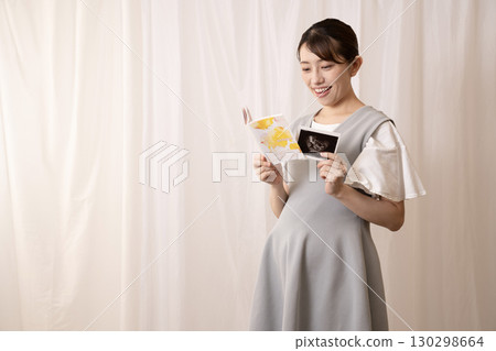 A pregnant woman looking at her maternal and child health handbook and ultrasound images 130298664