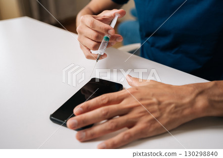 Close-up of technician using syringe needle to repair smartphone in professional workshop sitting at white table. Concept of delicate and precise nature of modern electronics repair. Close-up of technician using syringe needle to repair smartphone in professional workshop sitting at white table. Concept of delicate and precise nature of modern electronics repair. 130298840
