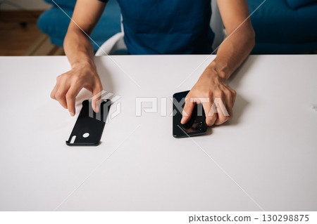 Closeup cropped shot of unrecognizable man inserting smartphone into protective case, ensuring secure fit sitting on white table at home. Concept of phone maintenance and service Closeup cropped shot of unrecognizable man inserting smartphone into protective case, ensuring secure fit sitting on white table at home. Concept of phone maintenance and service 130298875
