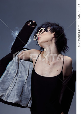 Woman wearing sunglasses and black dress poses dynamically with motion blur against dark background. 130299243