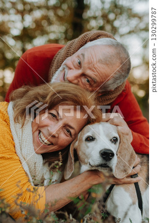 Elderly man and woman walking their dog in nature on autumn day. 130299787