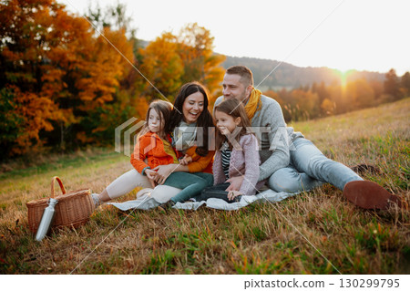 Parents with young children sitting outdoors in autumn light. 130299795