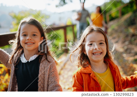 Sisters with parents in the background walking in park during warm autumn day. 130299823
