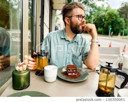 Bearded man sitting at outdoor cafe table looking to side. Modern lifestyle, urban leisure and relaxed atmosphere of everyday social environment. Bearded man sitting at outdoor cafe table looking to side. Modern lifestyle, urban leisure and relaxed atmosphere of everyday social environment. 130300061
