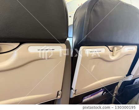 Airplane cabin interior with seatbacks showing safety labels. Air travel, passenger security and onboard aviation details. Airplane cabin interior with seatbacks showing safety labels. Air travel, passenger security and onboard aviation details. 130300195