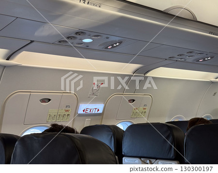Airplane cabin view with illuminated emergency exit sign and door. Passenger safety, flight security and aviation transport awareness. 130300197