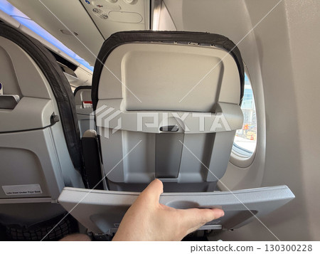 Passenger unfolding tray table on airplane seat. Practicality, space management, and in-flight comfort during air travel. Passenger unfolding tray table on airplane seat. Practicality, space management, and in-flight comfort during air travel. 130300228