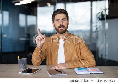 Confident man sitting in modern office, engaging in discussion while pointing upward Confident man sitting in modern office, engaging in discussion while pointing upward 130300633