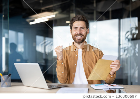 Modern office scene featuring a smiling man holding an envelope, expressing enthusiastic celebration. Represents achievement, success, and positive news in a professional and vibrant work environment 130300697