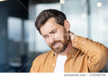 Stressed businessman experiencing neck pain, touching his neck with hand, showing discomfort and muscle tension, highlighting workplace health issues Stressed businessman experiencing neck pain, touching his neck with hand, showing discomfort and muscle tension, highlighting workplace health issues 130300749
