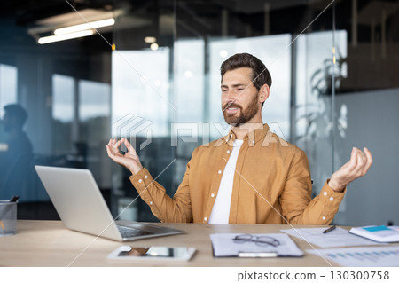 Office worker practicing mindfulness meditation at his desk with laptop, finding peace and balance during workday, promoting mental health and stress management in corporate environment 130300758