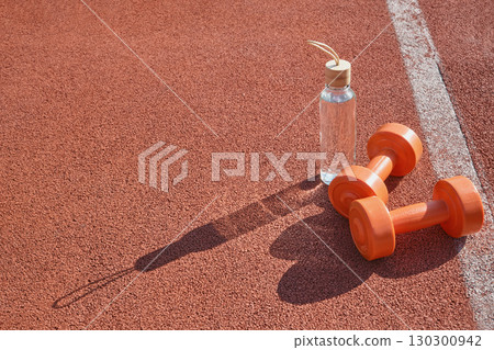 Reusable glass water bottle and dumbbells at stadium close-up 130300942