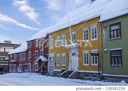 Vibrant traditional wooden houses in Troms, Norway display vivid colors against a snowy winter backdrop. Snow-covered streets enhance the charm of this picturesque Scandinavian town 130301258