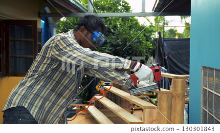 Carpenter securing wooden staircase steps with nail gun while wearing safety goggles and gloves 130301843