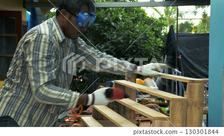 Carpenter fastening wooden staircase steps with pneumatic nail gun while wearing protective gloves and safety goggles 130301844