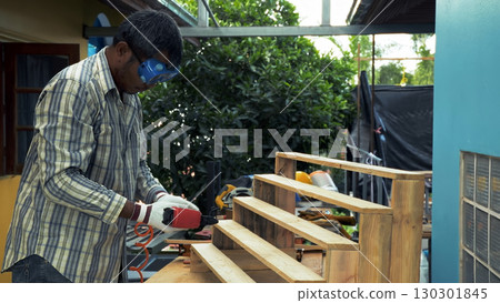 Carpenter securing wooden staircase frame with pneumatic nail gun while wearing protective gloves and safety goggles outdoors Carpenter securing wooden staircase frame with pneumatic nail gun while wearing protective gloves and safety goggles outdoors 130301845