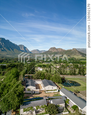 Mountains stand over peaceful rural setting, offering sense of seclusion from bustling city life. Tranquil countryside scene, greenery, agricultural fields, serene pond. Picturesque location, aerial 130302170
