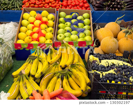 Fresh bananas with apples, melons, and grapes on colorful market display. Nutrition, agriculture, and seasonal harvest with diverse fruit assortment. 130302197