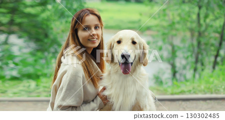Happy smiling owner woman with Golden Retriever dog sitting together on bench in summer park 130302485
