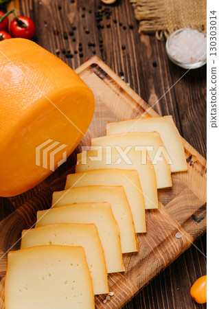 Round cheese wheel and sliced cheese on wooden board with rustic food ingredients 130303014