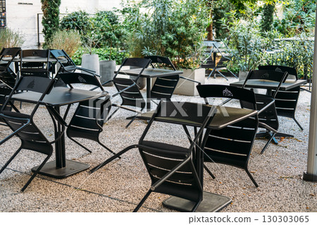 Empty outdoor cafe terrace with black metal chairs scattered around square tables. Urban greening, climate-conscious public design, European street culture, sustainability Empty outdoor cafe terrace with black metal chairs scattered around square tables. Urban greening, climate-conscious public design, European street culture, sustainability 130303065