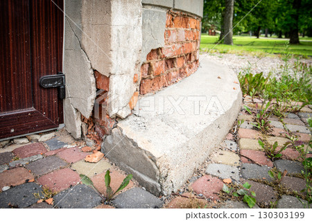 Damaged house foundation and cracked facade wall near entrance with visible bricks Damaged house foundation and cracked facade wall near entrance with visible bricks 130303199