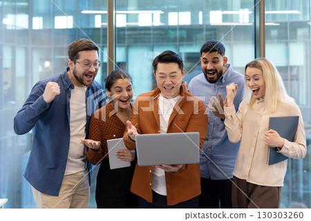 Euphoric multi-ethnic businesspeople are cheering and gesturing while looking at a laptop, celebrating a successful project or achievement in a modern office Euphoric multi-ethnic businesspeople are cheering and gesturing while looking at a laptop, celebrating a successful project or achievement in a modern office 130303260