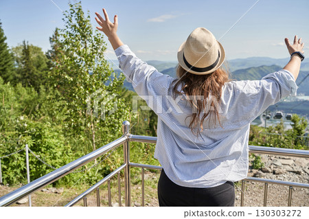 Young caucasian female enjoying scenic mountain view with arms raised 130303272