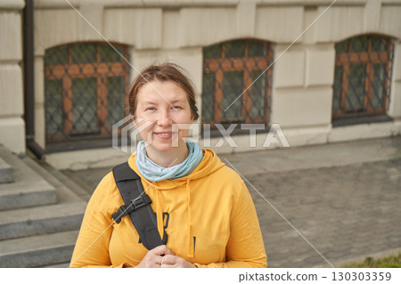 Smiling caucasian adult female wearing yellow hoodie outdoors with backpack 130303359
