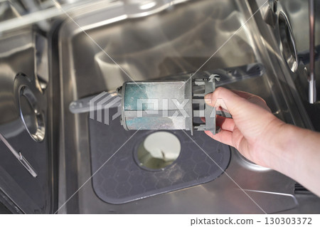 Hand holding dirty dishwasher filter over open dishwasher 130303372