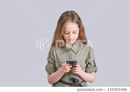 Caucasian young girl using smartphone in khaki dress against gray background 130303406