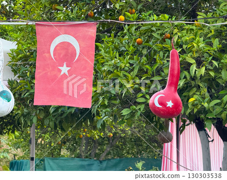 Turkish flag and decorative painted gourd hanging in garden. National identity, culture, and patriotic symbols in everyday outdoor environment. Turkish flag and decorative painted gourd hanging in garden. National identity, culture, and patriotic symbols in everyday outdoor environment. 130303538