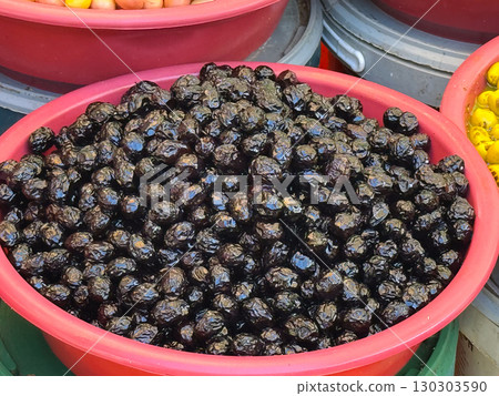 Close-up of shiny black olives in plastic bucket on market stall. Agriculture, farming, and seasonal fruit harvest with nutrition and healthy lifestyle. 130303590