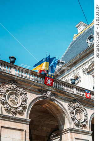Historic European building with Ukrainian and French flags under a clear blue sky. National identity, Ukraine solidarity, cultural diplomacy, European heritage Historic European building with Ukrainian and French flags under a clear blue sky. National identity, Ukraine solidarity, cultural diplomacy, European heritage 130303807