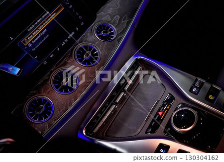 Close-up of car climate control panel with illuminated circular vents and metallic texture.  130304162