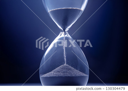 Hourglass filled with dark sand against a blue background captures the essence of time passing 130304479