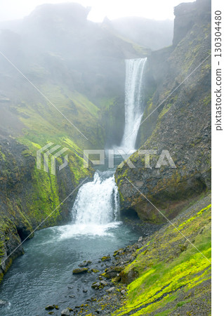 Beautiful cascading waterfalls in the lush landscapes of Iceland during foggy weather Beautiful cascading waterfalls in the lush landscapes of Iceland during foggy weather 130304480