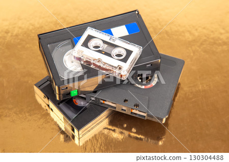 Vintage video and audio cassettes stacked on a reflective surface with golden background Vintage video and audio cassettes stacked on a reflective surface with golden background 130304488