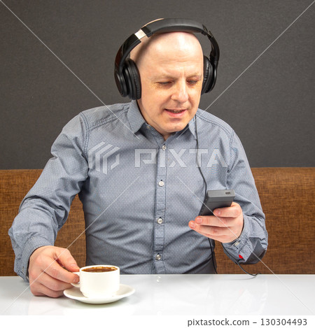 Man enjoying coffee while listening to music on a smartphone in a cozy cafe environment 130304493