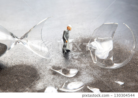 Miniature figure explores shattered hourglass on dark sand in creative art display Miniature figure explores shattered hourglass on dark sand in creative art display 130304544