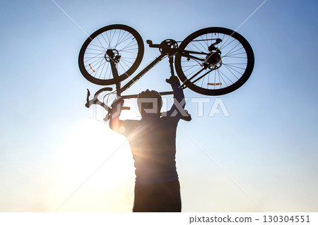 Cyclist celebrating victory at dusk with bicycle raised against the sunset sky 130304551